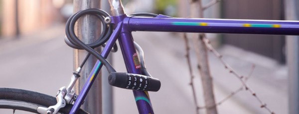 A purple bike frame locked up to a post using a combination cable lock