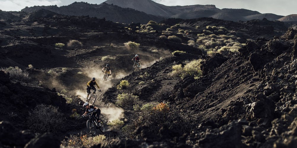 Four mountain bikers wearing ION clothing, riding through dusty terrain