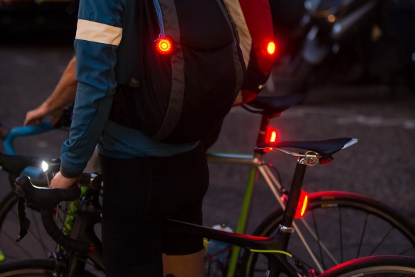 Road cyclists with rear lights mounted to backpacks and seat posts