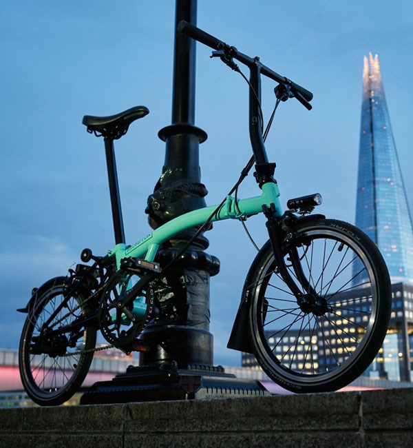 A Brompton Black bike with Turkish Green frame, propped against a lampost