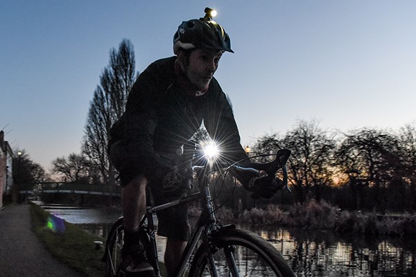 A road cyclist uses helmet and bar-mounted lights on a canal path