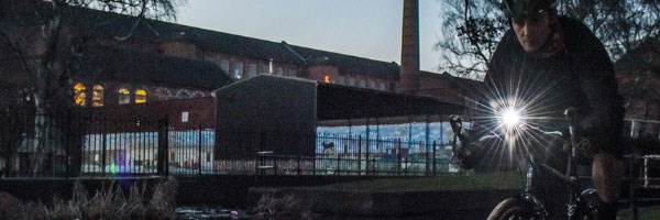 A cyclist riding next to a dark canal path with a bright Moon front light